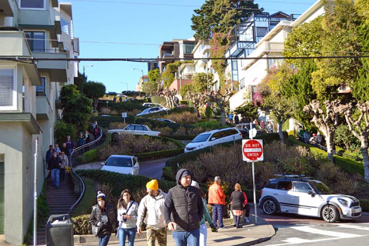 Lombard Street w San Francisco - najbardziej zakręcona ulica świata. Widok na ulicę z jej charakterystycznymi zakrętami i stromymi podjazdami, otoczoną przez zieleń i kolorowe domy.