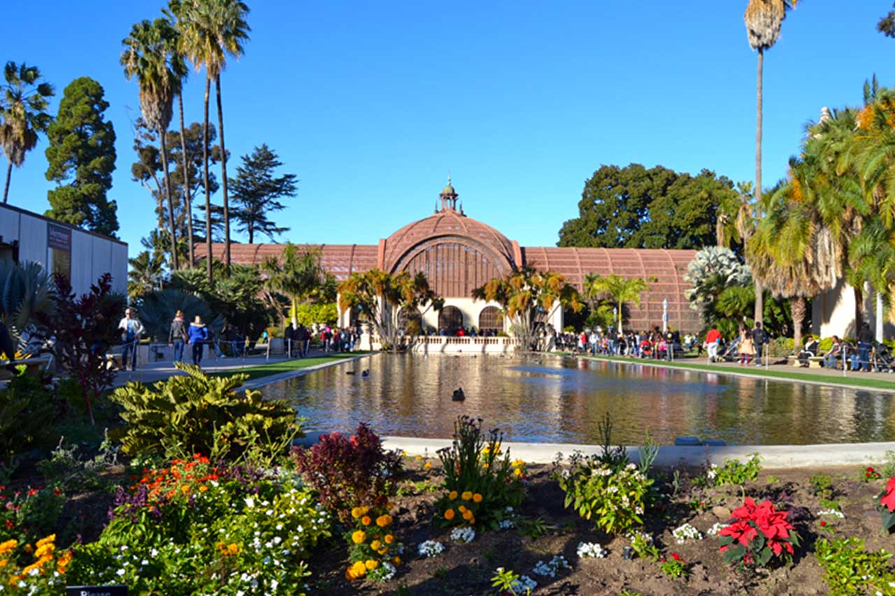 Botanical Building w Balboa Park w San Diego, otoczony palmami i kwiatami, z odbiciem w dużym stawie przed wejściem