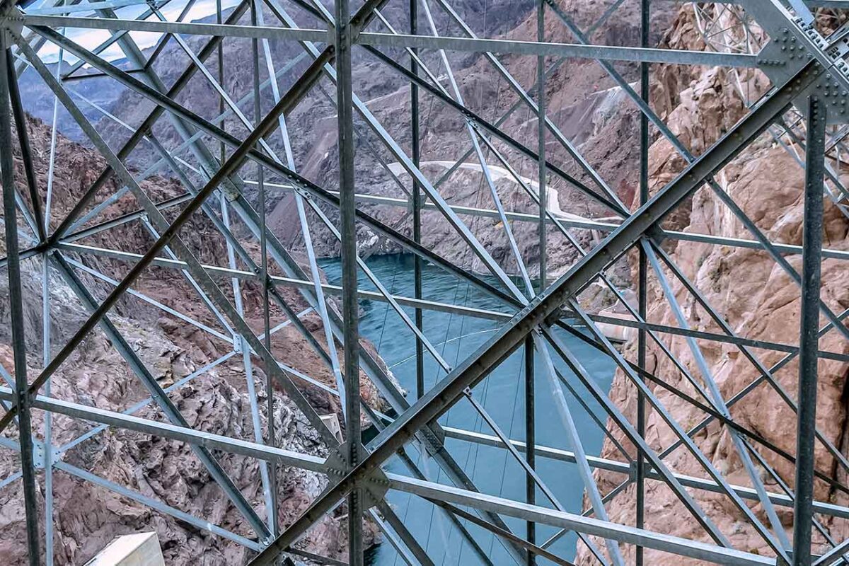 Spektakularny widok z Zapory Hoovera przez metalową konstrukcję na rzekę Colorado. Zdjęcie ukazuje inżynierię zapory na tle czerwonych skał kanionu Nevada-Arizona.