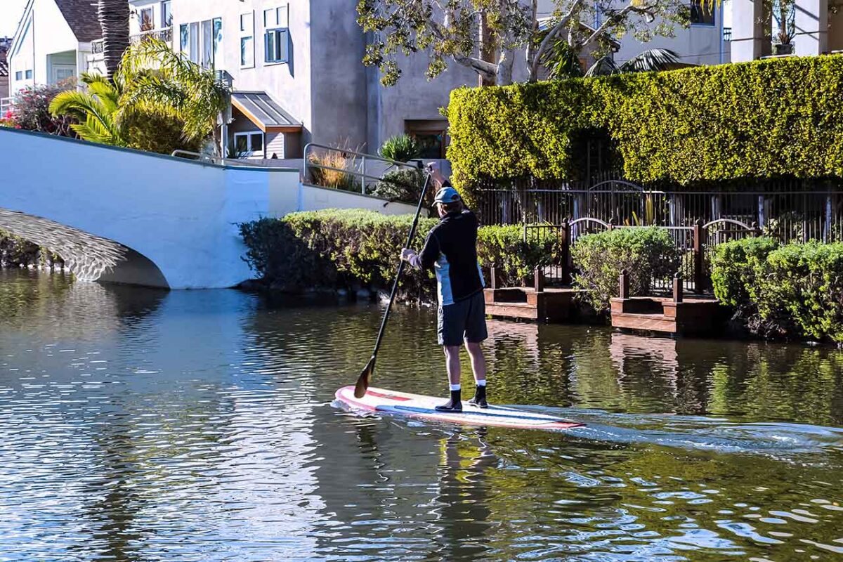 Osoba na paddleboardzie pod niebieskim mostem