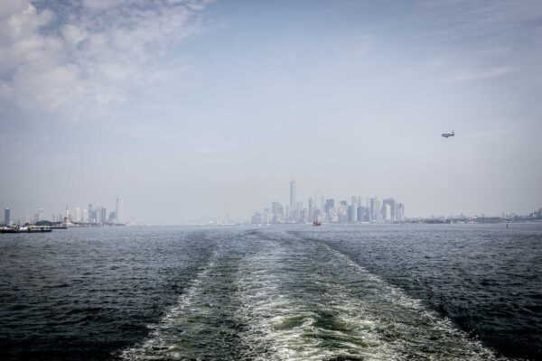 Widok na oddalające się wieżowce Nowego Jorku w tle, z wodami Upper New York Bay na pierwszym planie, podczas rejsu na Staten Island.