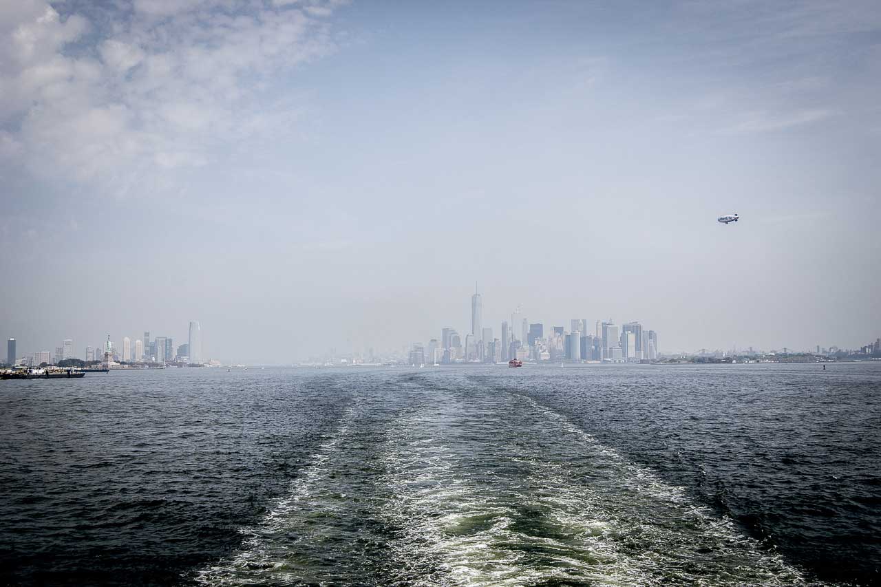 Widok na oddalające się wieżowce Nowego Jorku w tle, z wodami Upper New York Bay na pierwszym planie, podczas rejsu na Staten Island.