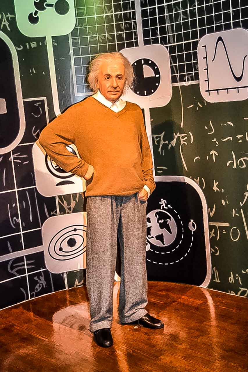 Albert Einstein in maglione davanti a una lavagna con formule matematiche.