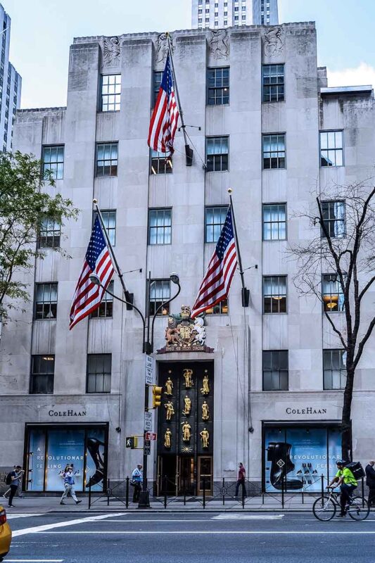 Główna fasada Rockefeller Center z rzędami flag amerykańskich i drzewami w tle