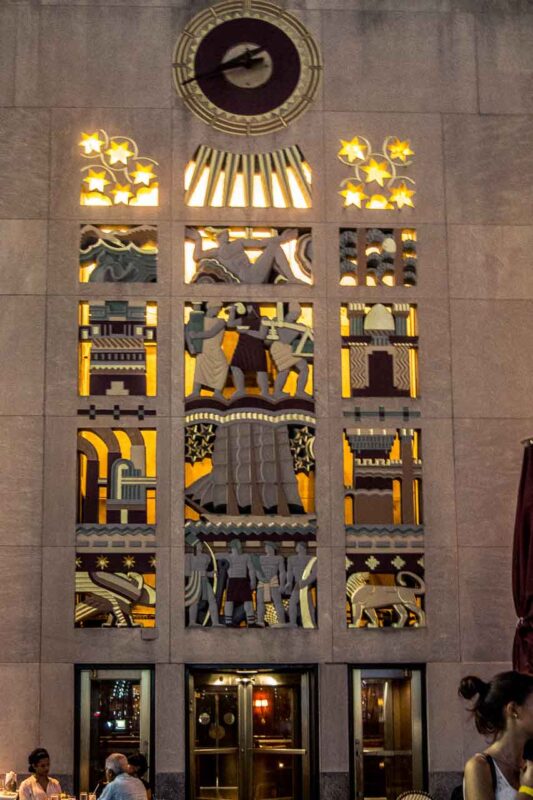 Ozdobny zegar nad iluminowanym wejściem w Rockefeller Center