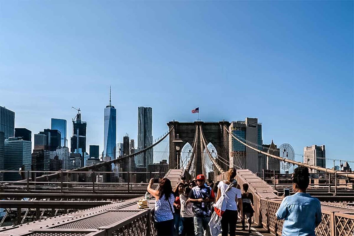 Ludzie spacerujący po Brooklyn Bridge z panoramą Manhattanu w tle