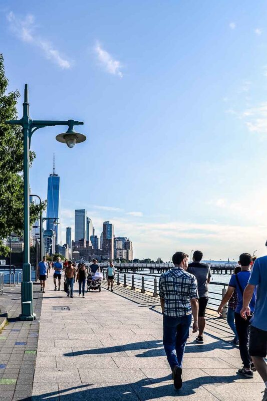Ludzie spacerujący promenadą Hudson River Park z widokiem na One World Trade Center