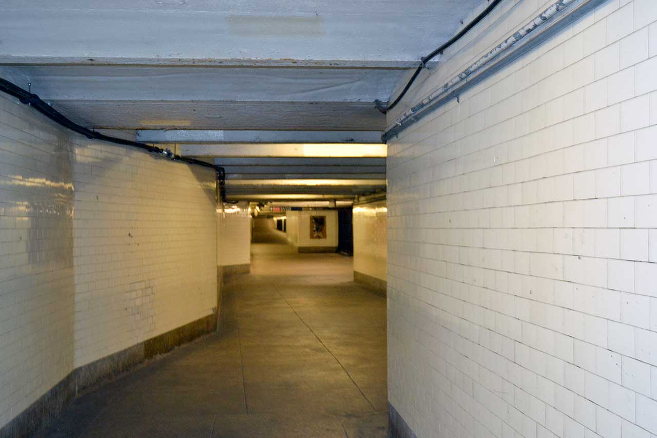 Corridoio sotterraneo della metropolitana di New York Lungo corridoio sotterraneo nella metropolitana di New York con pareti rivestite di piastrelle bianche