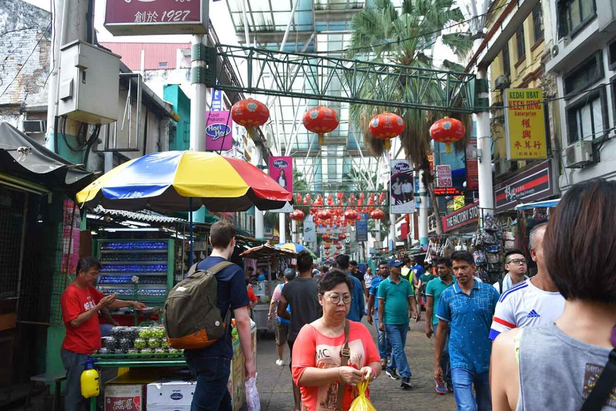 Zdjęcie uchwyca żywiołową atmosferę Petaling Street Market w Kuala Lumpur, gdzie tradycja spotyka się z nowoczesnością na tle kolorowych straganów i ulicznego jedzenia.
