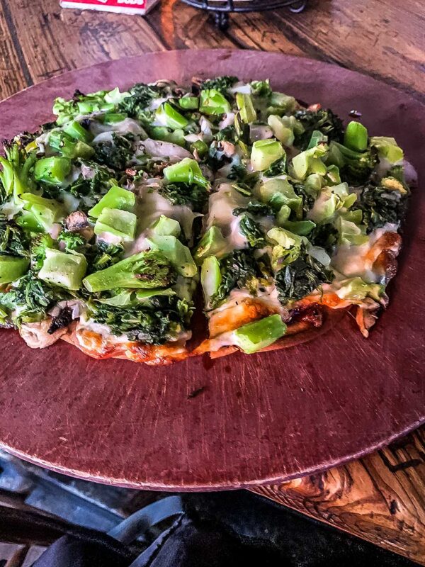 Una grande pizza servita su un vassoio colorato al bancone del No Name Pub.