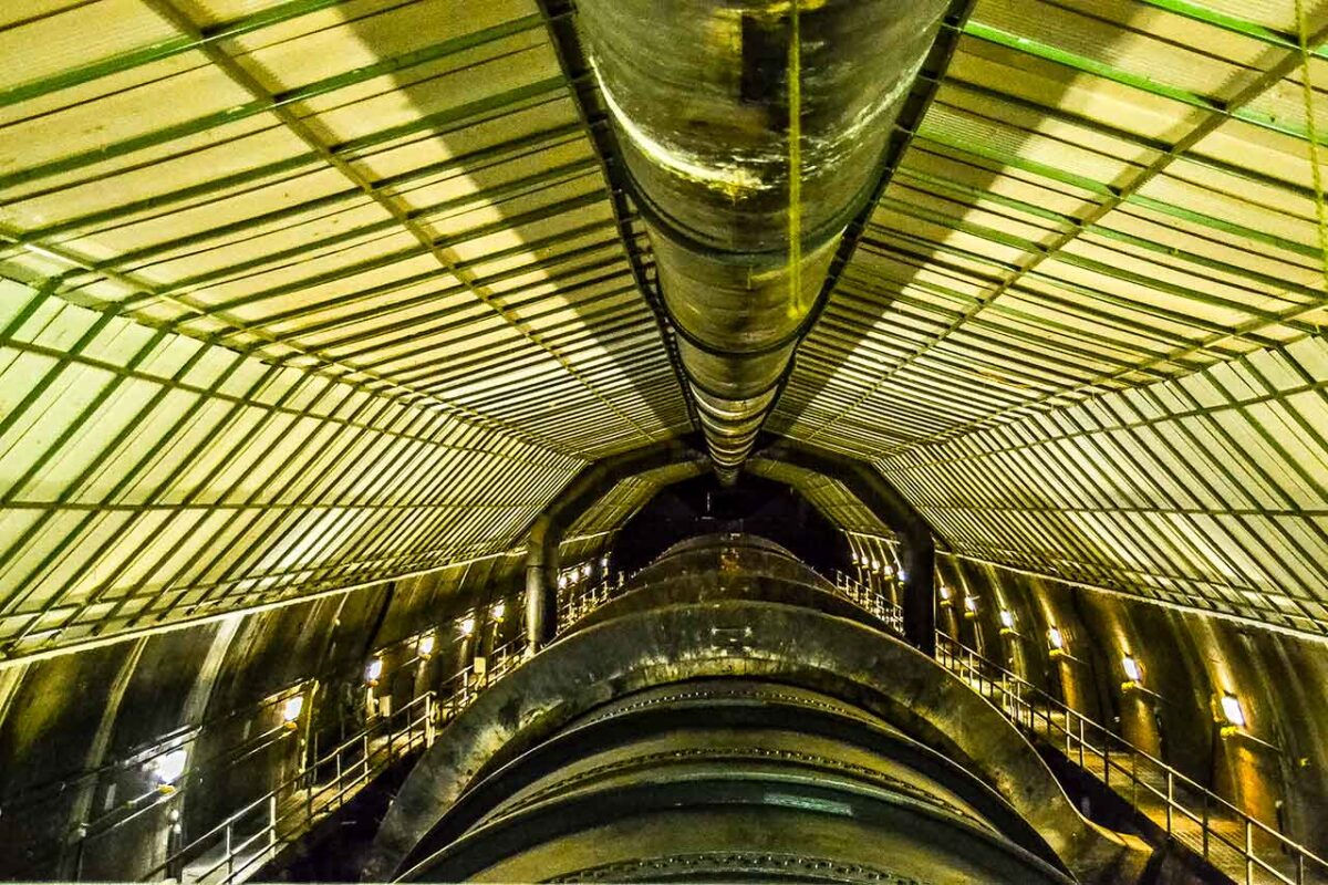 Długi prosty tunel wewnątrz Zapory Hoovera z łukowym betonowym sufitem, metalowymi balustradami i rzędami lamp oświetleniowych