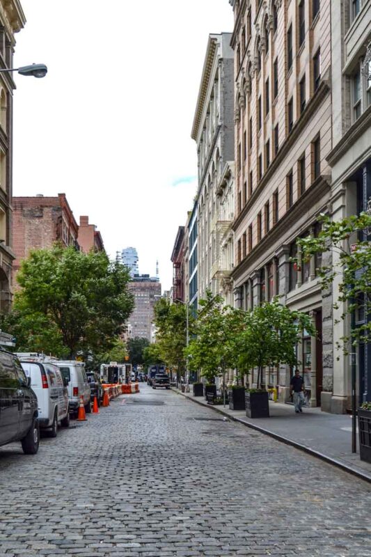Suggestiva strada acciottolata a SoHo, New York, con i caratteristici blocchi belgi, circondata da edifici storici e boutique.
