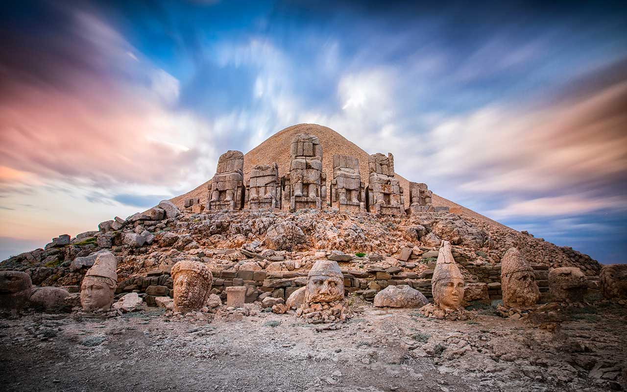 Wschodni taras Góry Nemrut o wschodzie słońca z Wielkim Ołtarzem na tle posągów i tumulusu. Miejsce wpisane na Listę Światowego Dziedzictwa UNESCO, gdzie rzekomo spoczywa król Antioch z Kommagene.