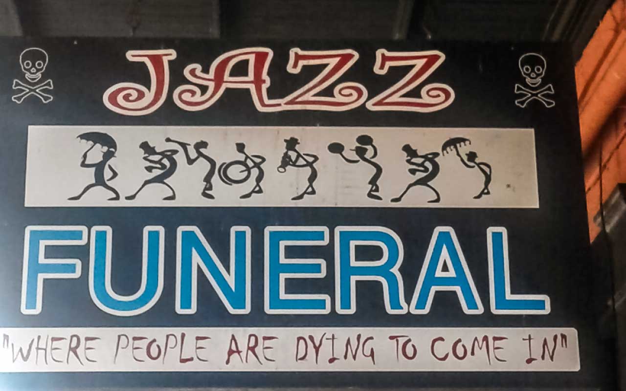 Insegna con la scritta "Jazz Funeral" e il motto "Where people are dying to come in".