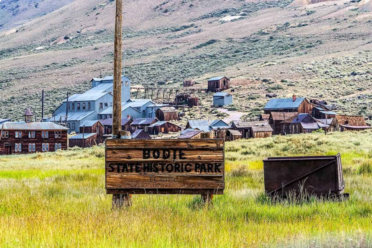 Insegna in legno del Bodie State Historic Park con vista sugli edifici abbandonati della città fantasma.