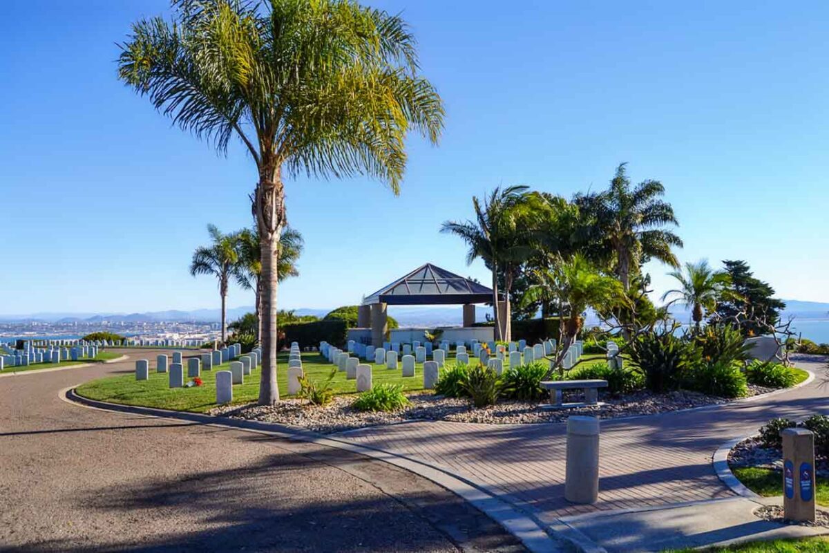 Vista dell’ingresso del cimitero Fort Rosecrans a San Diego con palme, padiglione e una fila di lapidi bianche