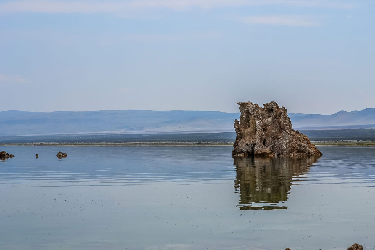 Roccia tufacea isolata nel Mono Lake riflessa sulla superficie calma dell’acqua.